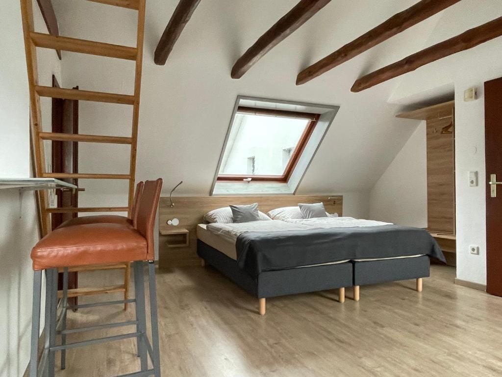 A bedroom with a loft bed, a wooden ladder, a skylight, and a wooden door.