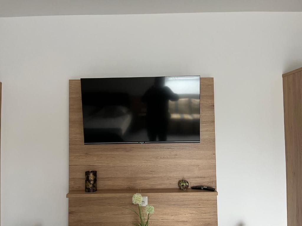 Ein Flachbildfernseher an einer Holzwand montiert, darunter ein Regal.