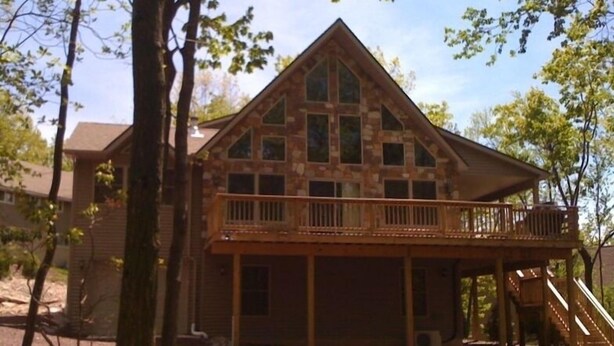 Une cabane en rondins à deux étages, dotée d’un balcon et d’un escalier menant à une terrasse.