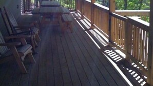 Une terrasse en bois, agrémentée d’une table et de chaises, entourée d’une rambarde et offrant une vue sur une zone boisée.