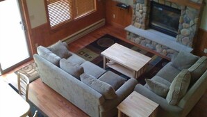 Un salon chaleureux avec une cheminée en pierre, un plancher en bois et un grand canapé d’angle.