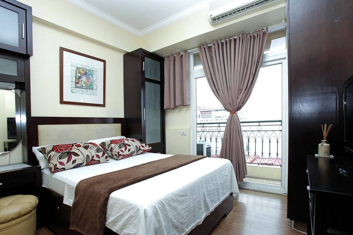 Une chambre d’hôtel avec un lit, un bureau, une chaise, une télévision et un balcon avec des rideaux.