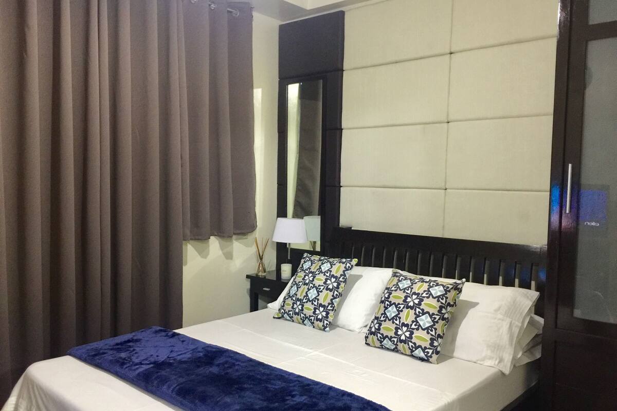 Une chambre d’hôtel avec un grand lit, une tête de lit, une table de chevet, une lampe et un miroir.