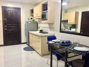 A compact kitchen with a refrigerator, microwave, and a dining area with a table set for two. - MCH Suites at Le Mirage De Malate (Manila)