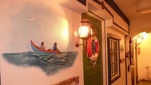 A hallway with a mural of a boat on water, a green door, and a wall-mounted light fixture. - Sopperogården - Hostel (Övre Soppero)