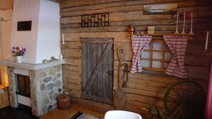 A rustic cabin interior with a stone fireplace, wooden walls, a wooden door, and a large wheel. - Sopperogården - Hostel (Övre Soppero)