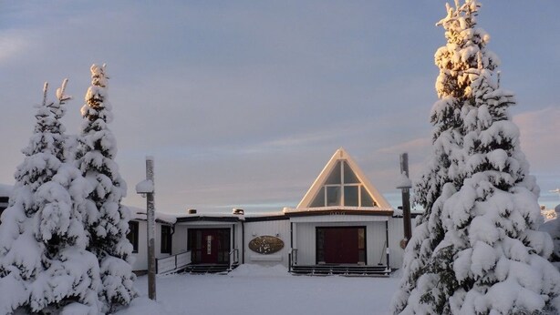 A snow-covered building with a triangular roof and a central entrance. - Sopperogården - Hostel (Övre Soppero)