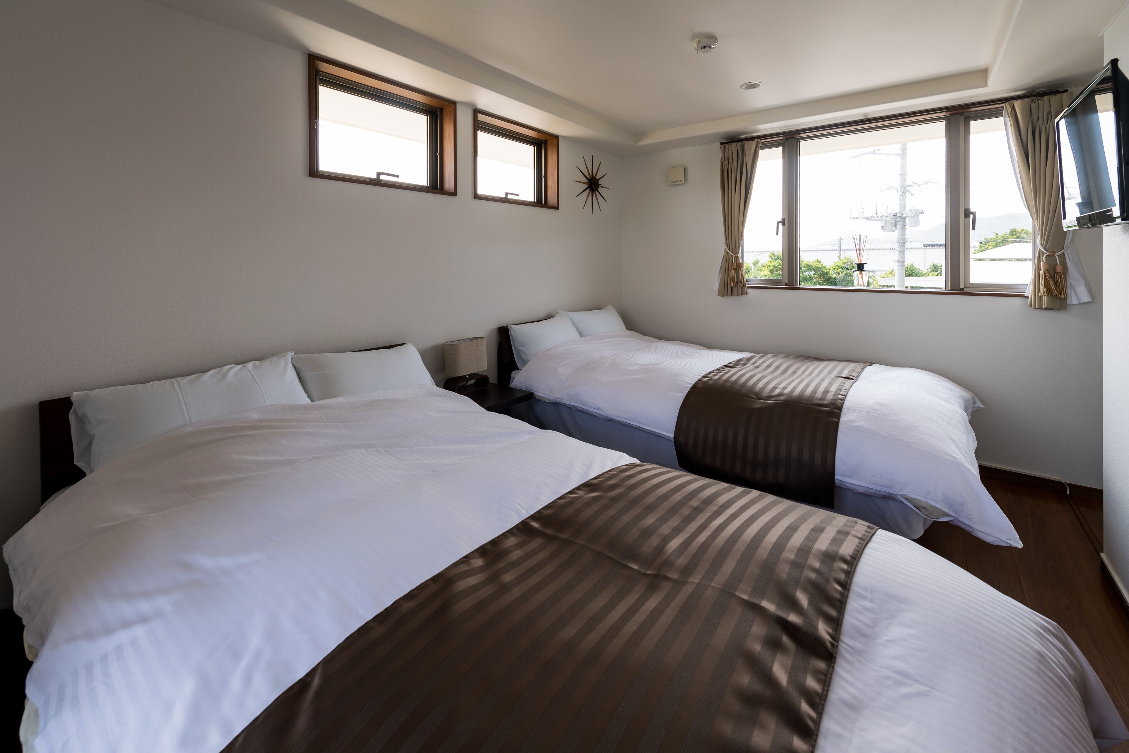 A hotel room with two beds, a TV, and large windows with curtains.