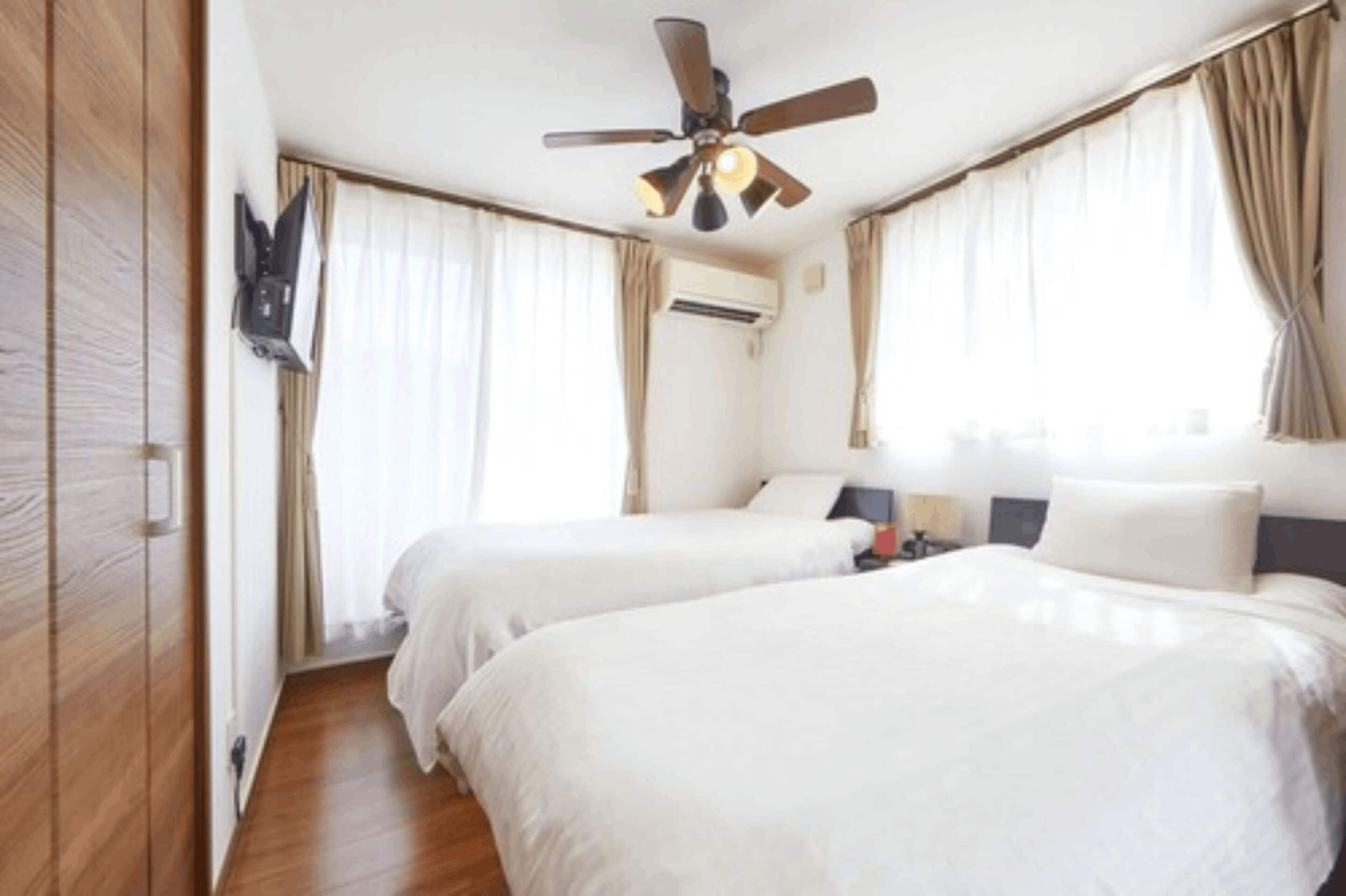 A hotel room with two beds, a ceiling fan, and a mounted TV.