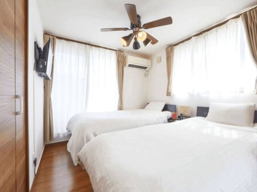 A hotel room with two beds, a ceiling fan, and a mounted TV.