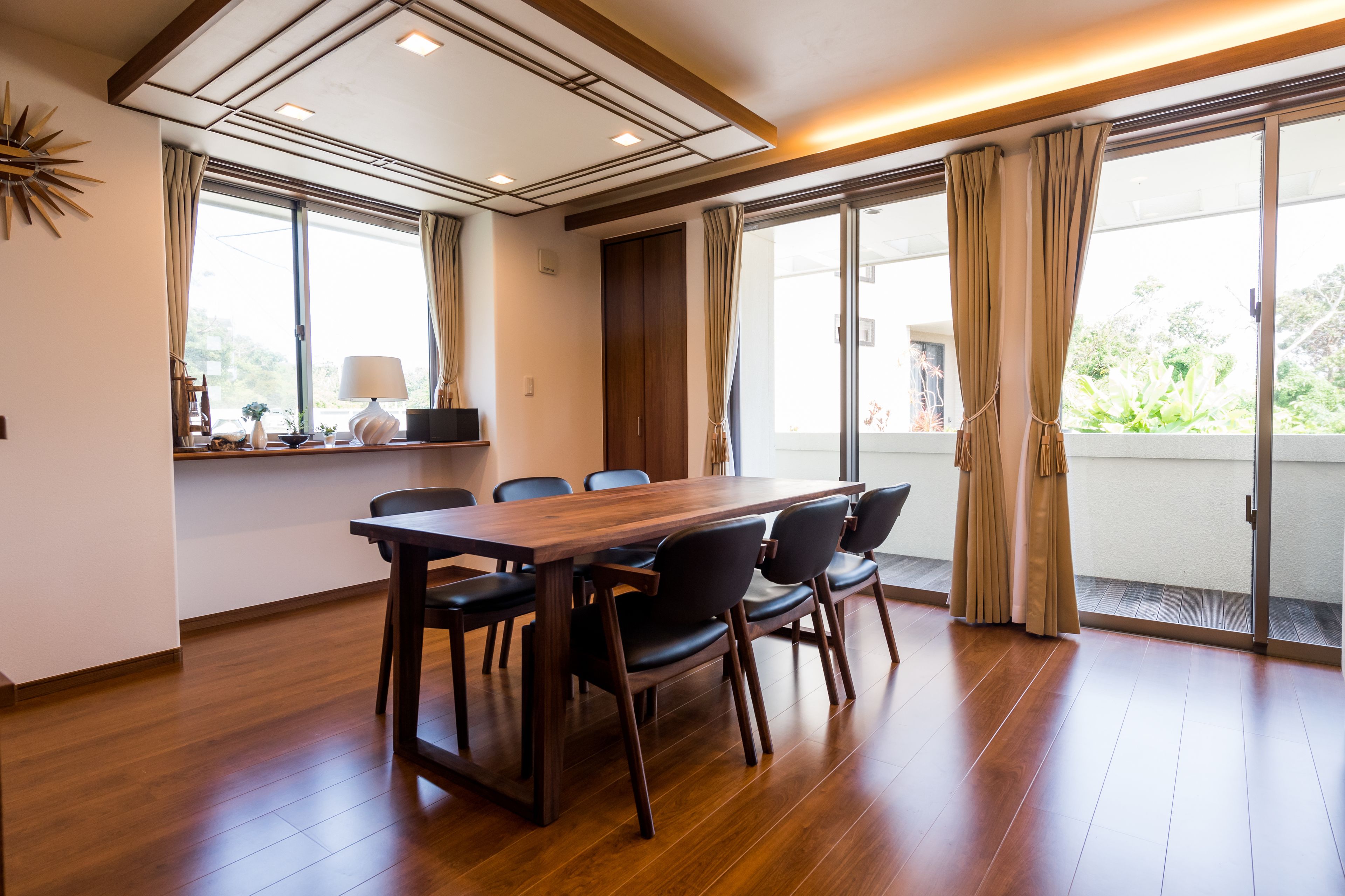 A conference room with a wooden table and chairs, large windows with curtains, and a ceiling with recessed lighting.