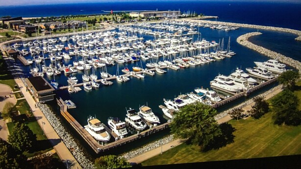 Une vue aérienne d’une marina où de nombreux bateaux sont amarrés, entourée de verdure et sous un ciel dégagé.