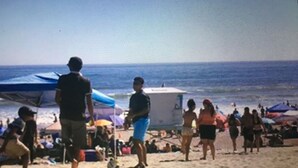 Une scène de plage où l’on voit des gens qui marchent et qui sont debout.