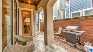Un patio al aire libre con mobiliario de mimbre, una parrilla y una puerta que da a una zona cubierta.