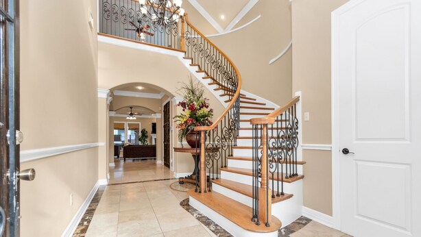Un pasillo amplio con una escalera de madera, una puerta blanca y una planta decorativa.