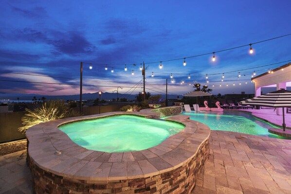 A swimming pool with a hot tub, lounge chairs, and string lights.