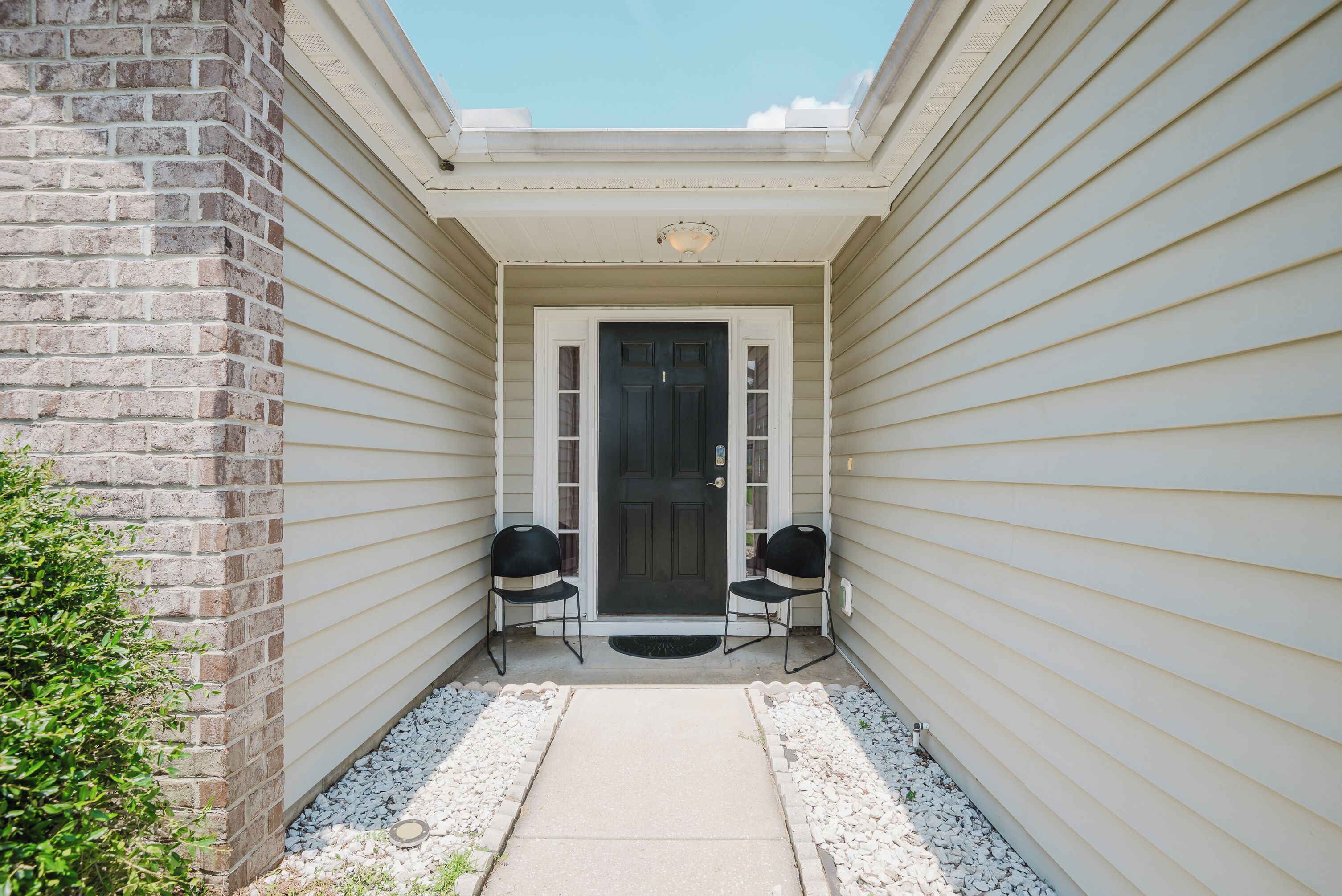 A house entrance with a front door, two chairs, and a small pathway.