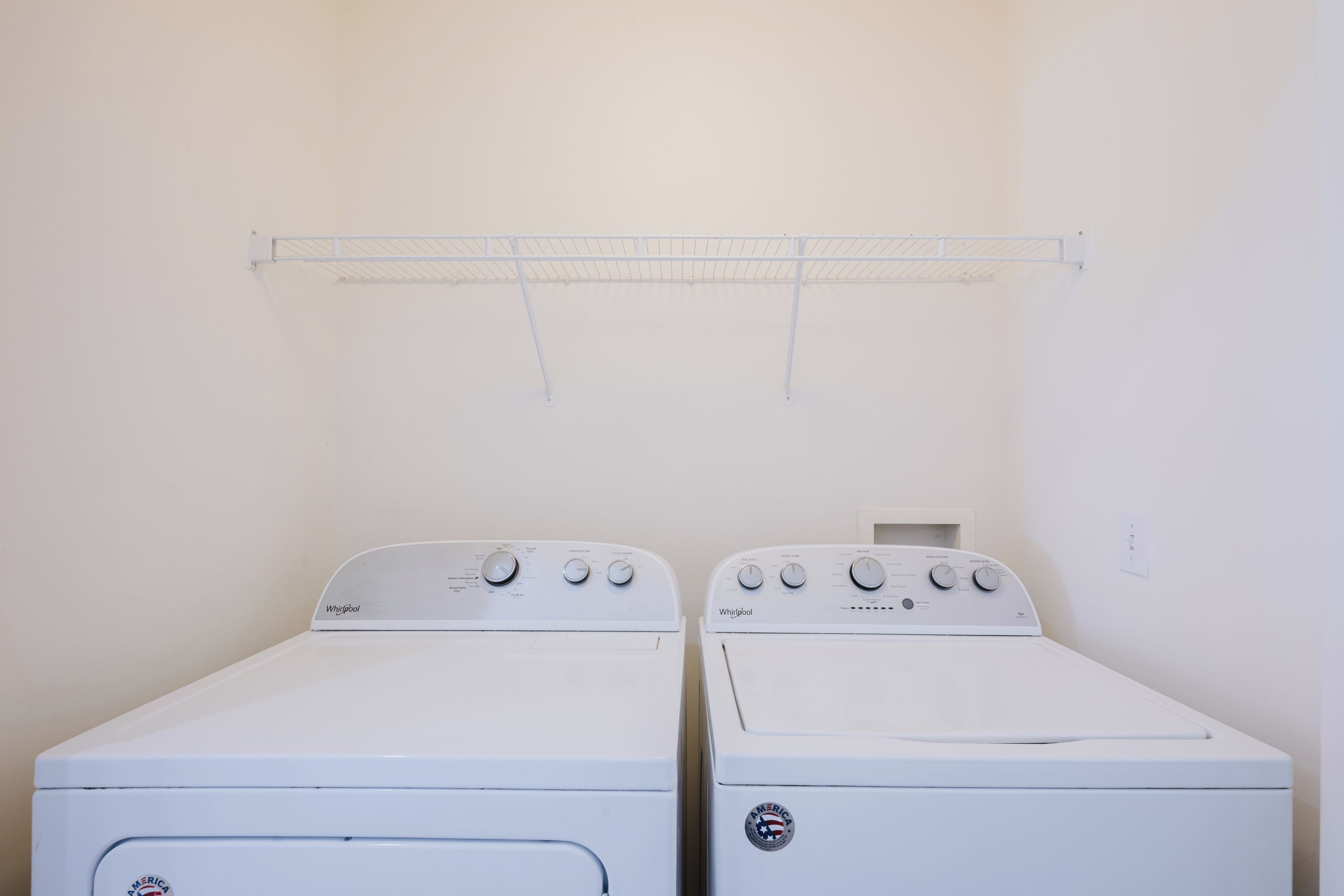 Deux lave-linge Whirlpool blancs se trouvent dans une buanderie, avec un étendoir métallique placé au-dessus.