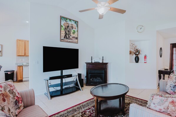 A living room with a flat-screen TV, a fireplace, a ceiling fan, and a clock on the wall. - Blufton, Hilton Head Is SC. Vacation home. 3BR. 2BA Sleeps 6. 1 Night Min Stay. (Bluffton)