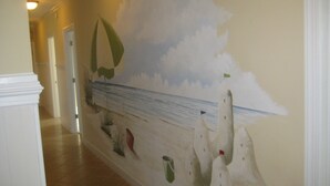 En gang med et mural, der viser en sejlbåd på havet, et fyrtårn og nogle planter.