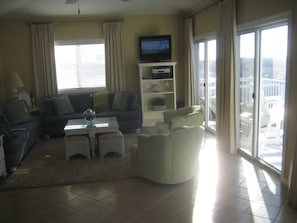 Un soggiorno con divano, poltrone, tavolino e televisore. Include un balcone con ringhiera e vista sulla città.
