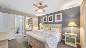 Una habitación de hotel con cama, lámparas de noche, ventilador de techo y mesita de noche.