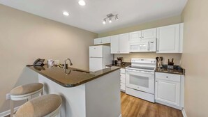 Cocina compacta con armarios blancos, una isla central con taburetes, microondas y estufa.