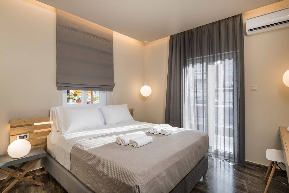 A modern hotel room with a large bed, a desk, and a window with curtains.