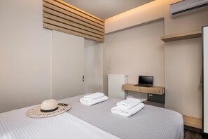 A hotel room with a bed, a television on a wooden shelf, a radiator, and a hat on the bed. - Sun Ray Luxury Apartments (Chania)