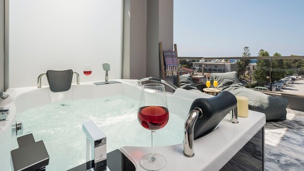 A modern bathroom with a bathtub, a glass of red wine, and a towel rack. - Sun Ray Luxury Apartments (Chania)