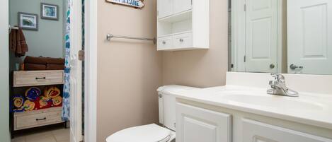 A bathroom with a white toilet, a sink with a chrome faucet, and a cabinet above the sink. There are towels stacked on a shelf and a sign on the wall.