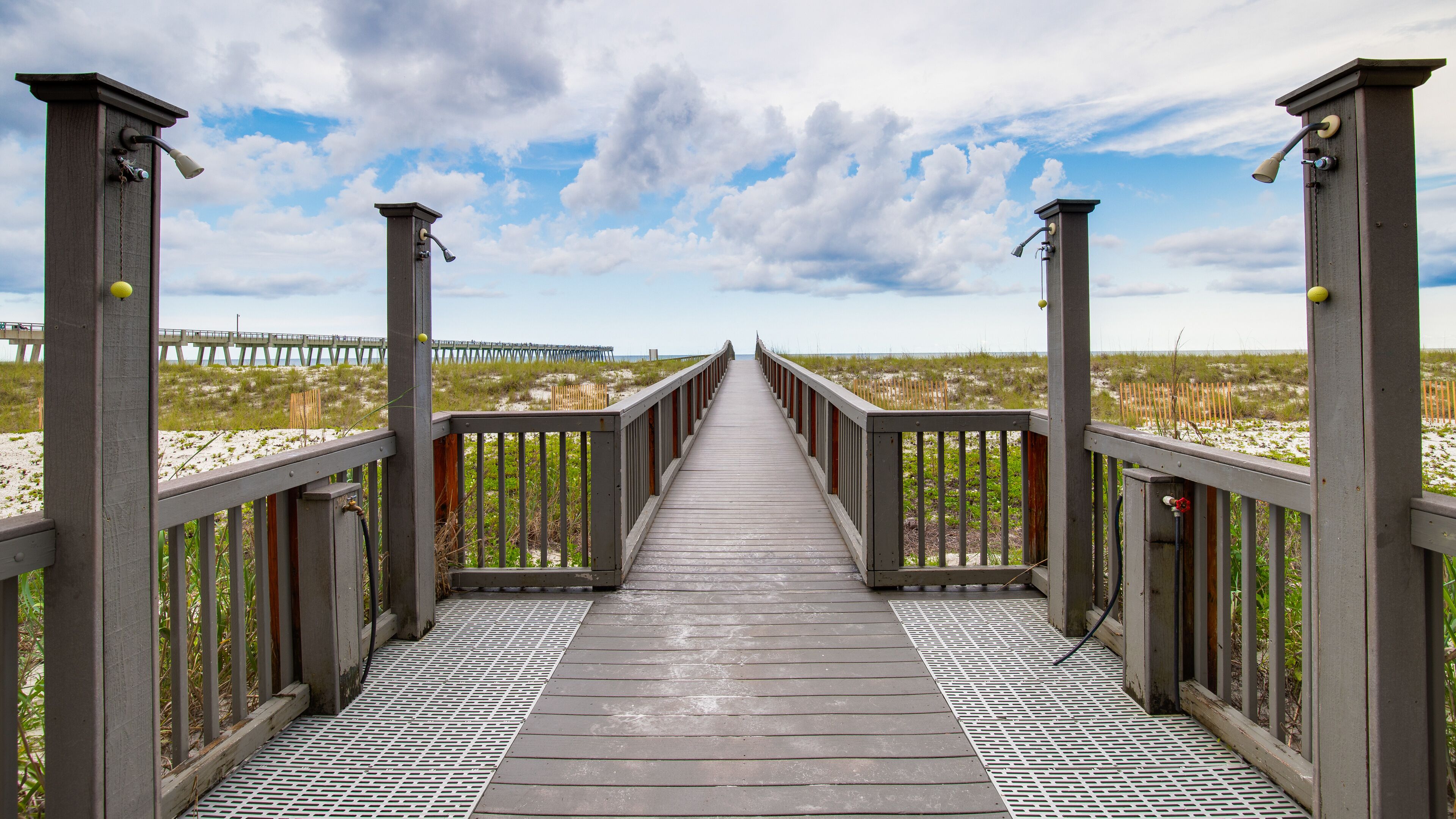 A wooden boardwalk leading to a beach with a pier in the distance.