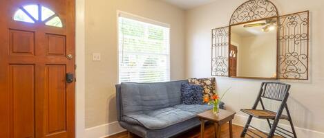 A room with a wooden door, a gray sofa, a small table with a vase, and a chair.