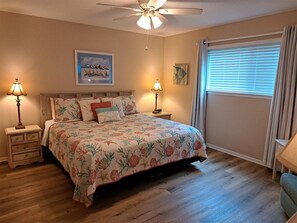 A bedroom with a bed, two bedside tables, a ceiling fan, a window with blinds, and artwork on the wall. - Lazy Days #801 Beach Service Included-2 Chairs and Umbrella 2Bd 2-Bath 1st Fl (Destin)