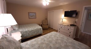 A bedroom with two beds, a television, a chair, and a dresser.