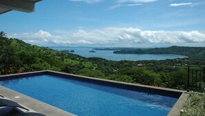 A swimming pool with a view of a coastal landscape, including hills and a body of water. - Villa Santaluz - Magnificent Ocean View Villa (Coco)