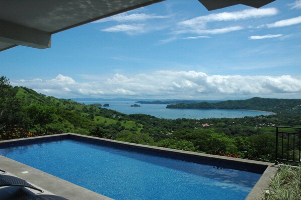 A swimming pool with a view of a coastal landscape, including hills and a body of water.