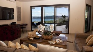 A spacious living room with a large window offering a view of the sea and mountains. - Villa Santaluz - Magnificent Ocean View Villa (Coco)