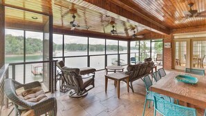 A spacious indoor area with a large window overlooking a body of water, furnished with wicker chairs and a wooden table.