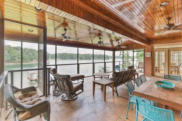 A spacious indoor area with a large window overlooking a body of water, furnished with wicker chairs and a wooden table.