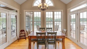 A dining room with a large table and chairs, large windows, and a chandelier.