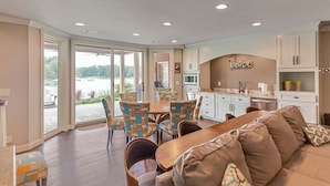 A spacious living area with a dining table, colorful chairs, a sofa, and a kitchen area with a sign that reads "Theatre".