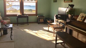 A living room with a piano, a television, and a window with a view of the ocean. - Amazing sunset in front of historic house  (Blaine)
