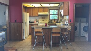 A kitchen with wooden cabinets, a central island with bar stools, a stove, and a washing machine in the corner. - Amazing sunset in front of historic house  (Blaine)