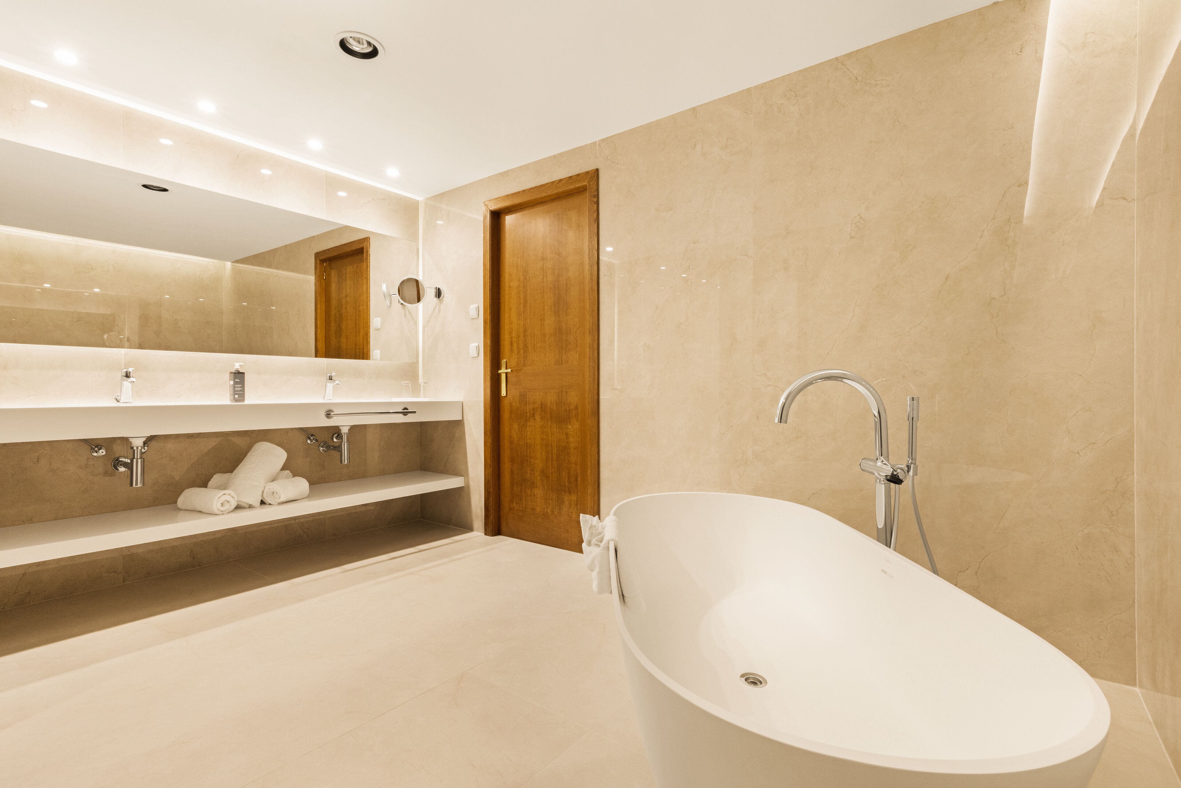 Un baño moderno con una bañera independiente, una puerta de madera y un tocador con espejo y perchero.