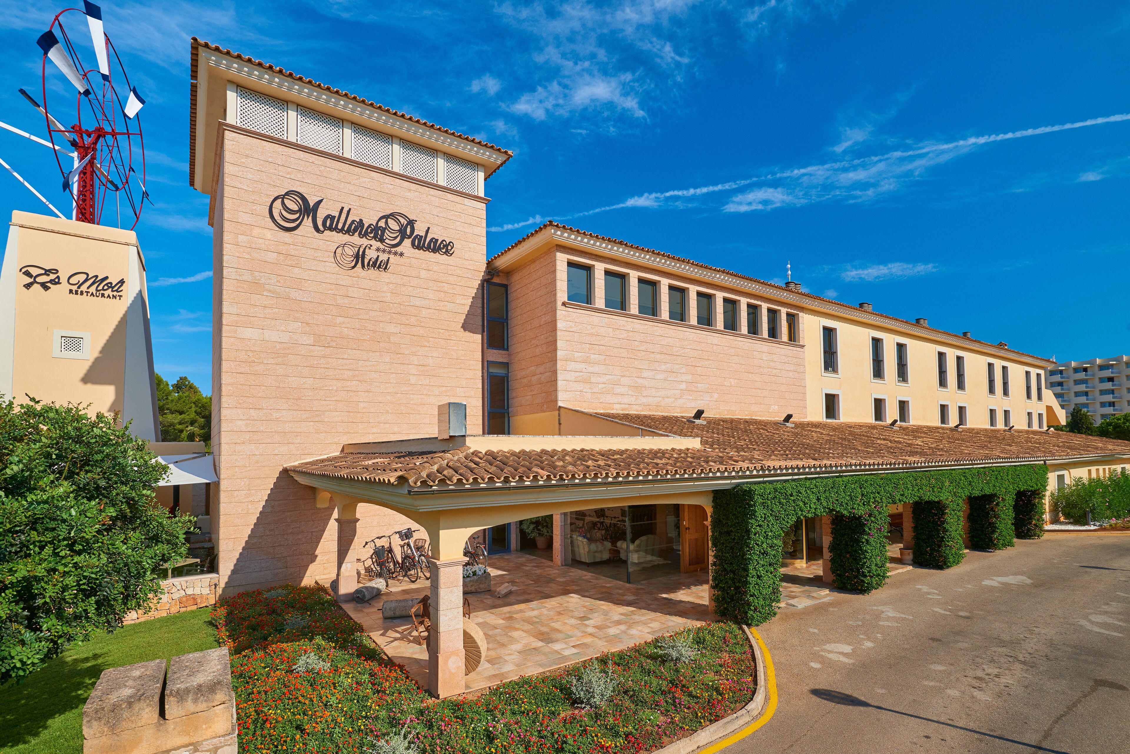 Un hotel con un cartel llamativo, un espacio exterior cubierto y un jardín ajardinado.