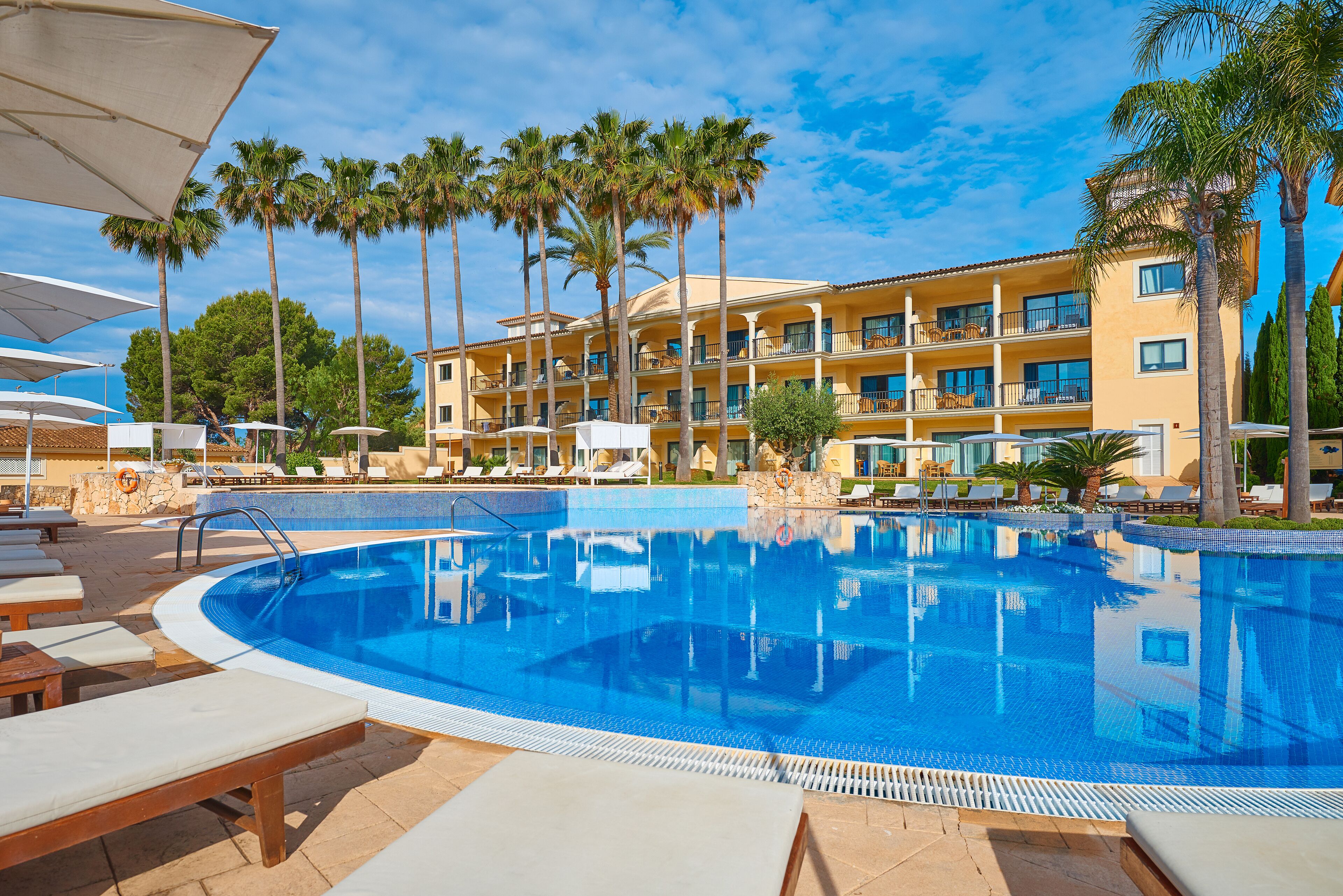 A swimming pool with lounge chairs, palm trees, and a hotel building in the background.