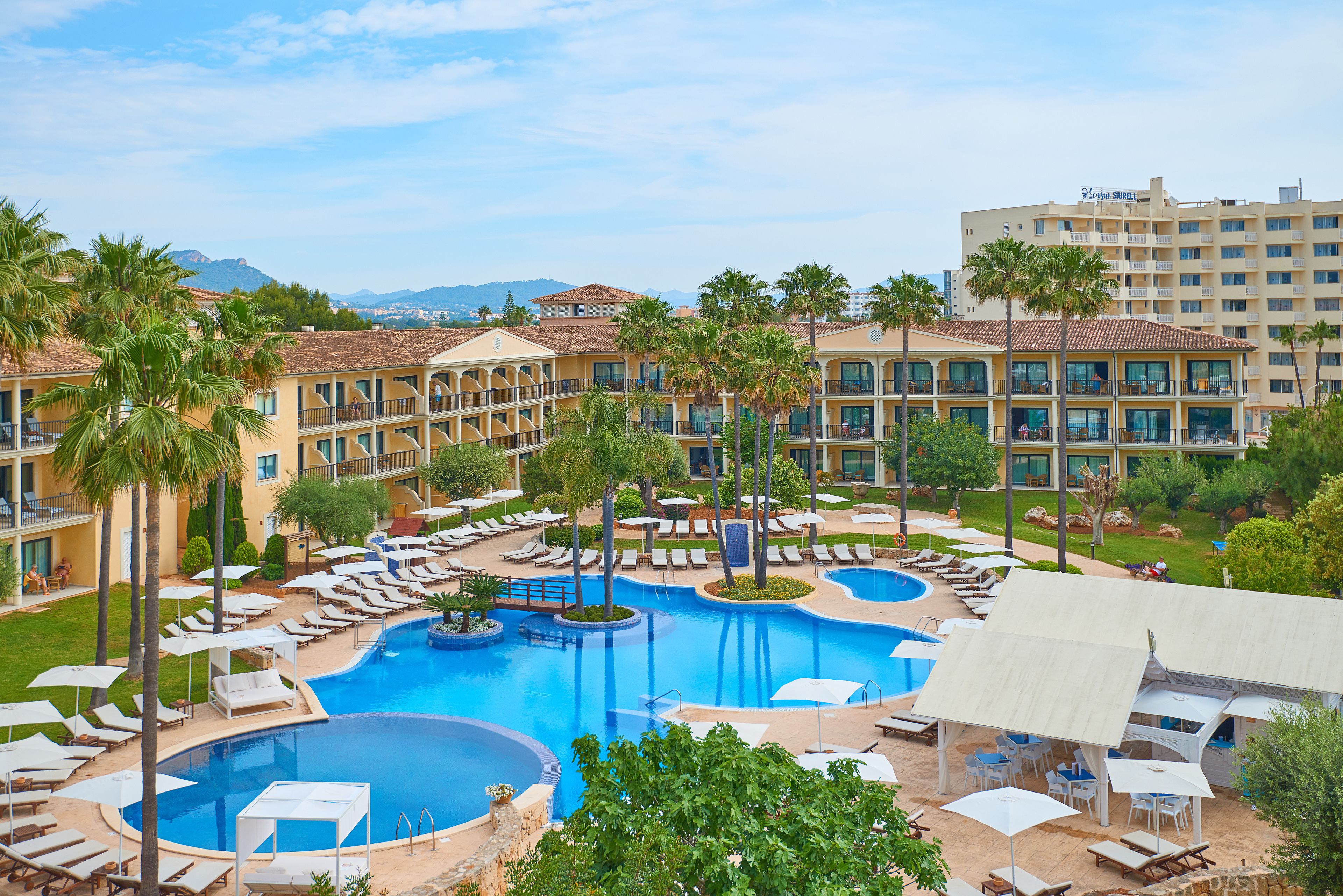 Un hotel con un amplio espacio de piscina, numerosas tumbonas y palmeras.