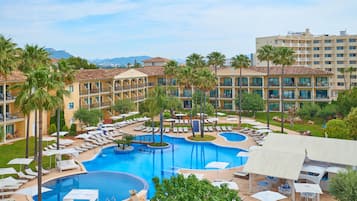 Un hotel con un amplio espacio de piscina, numerosas tumbonas y palmeras.