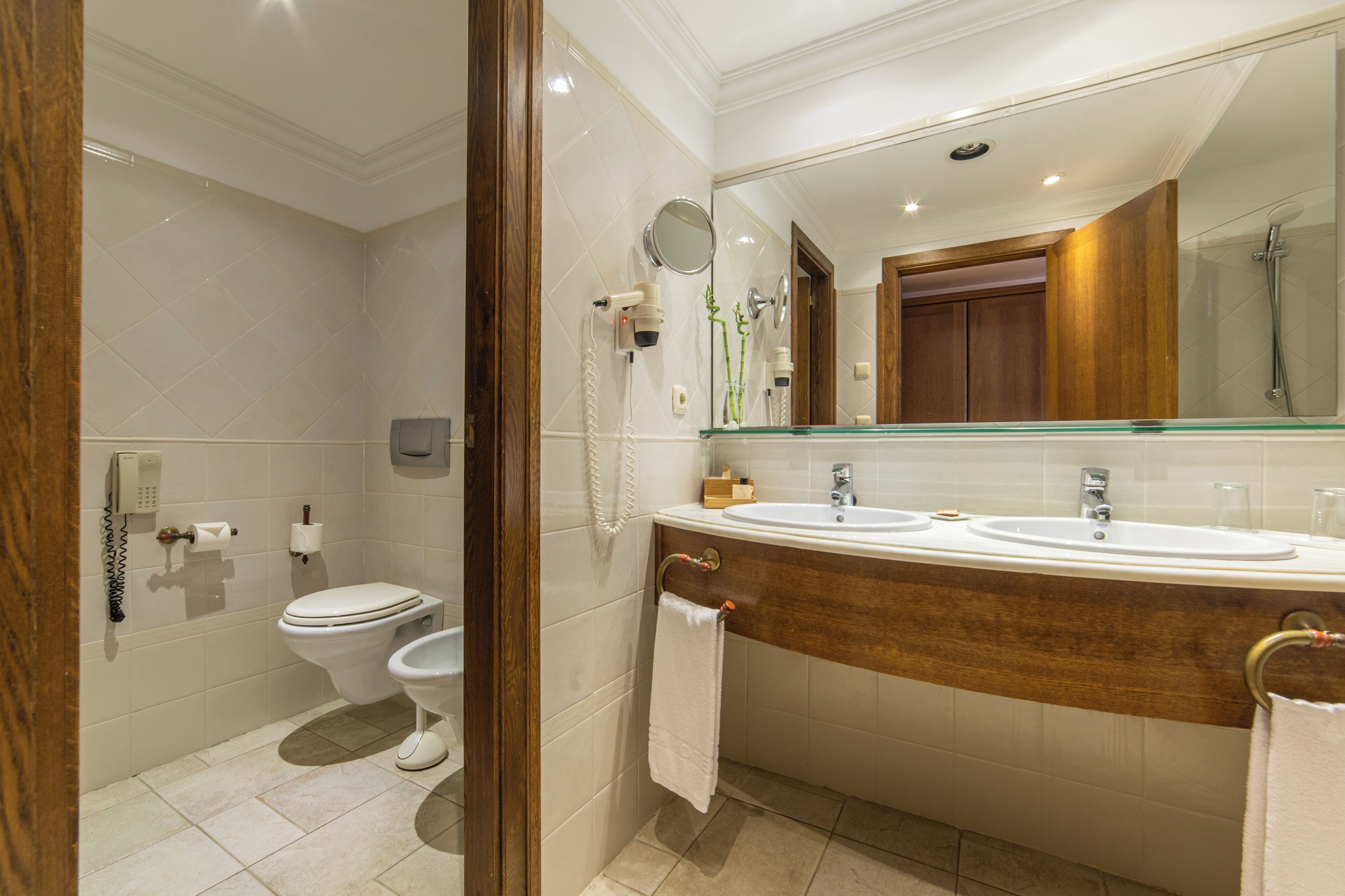 Ein Badezimmer mit Toilette, Bidet, zwei Waschbecken, einem Spiegel und einer Dusche.